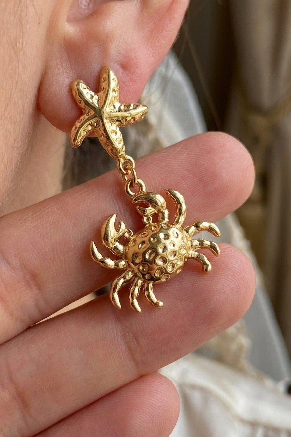 Gold drop earrings featuring a textured starfish stud and a dangling crab pendant.