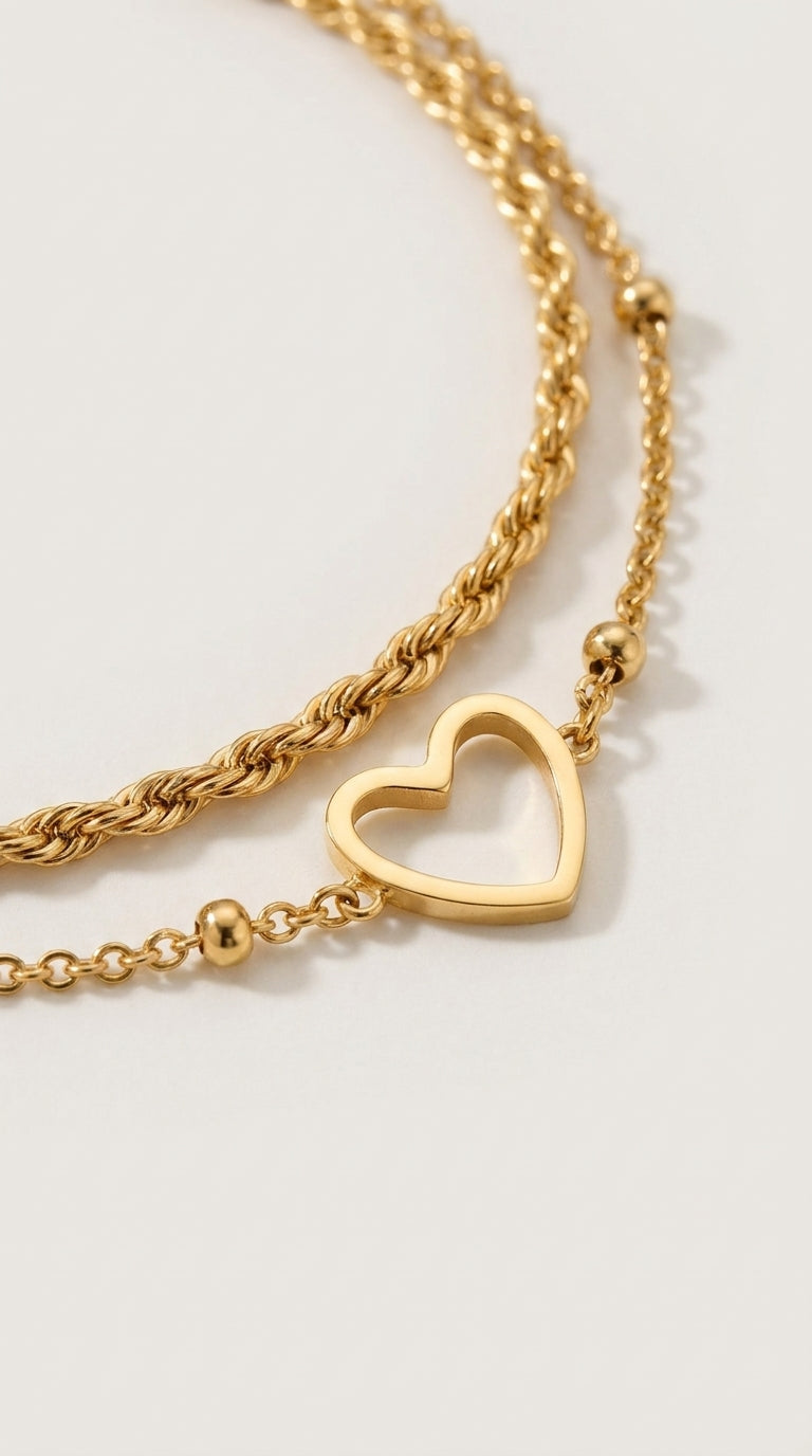 Layered gold chain bracelet with a twisted chain, a delicate link chain, small beads, and an open heart charm.