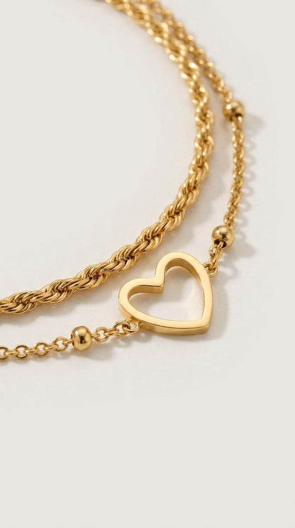 Layered gold chain bracelet with a twisted chain, a delicate link chain, small beads, and an open heart charm.