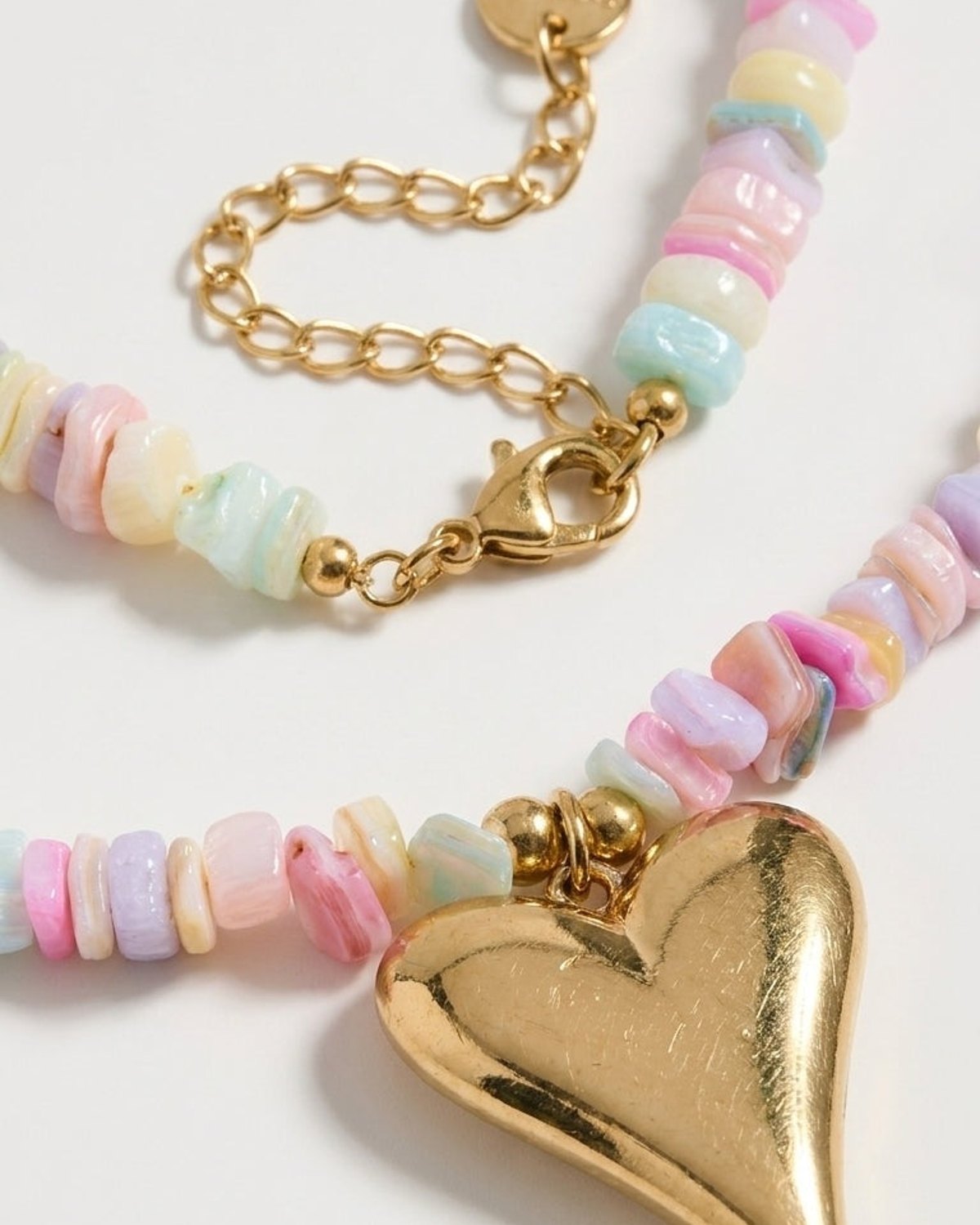 A necklace featuring pastel-colored chip beads and a large gold heart pendant on a chain.
