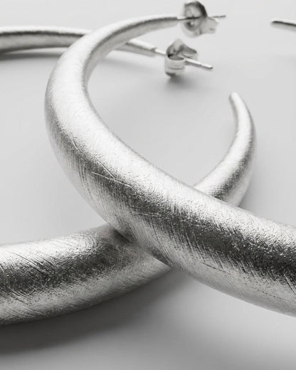 Textured silver hoop earrings with a brushed finish and post backs, in a modern, organic style.