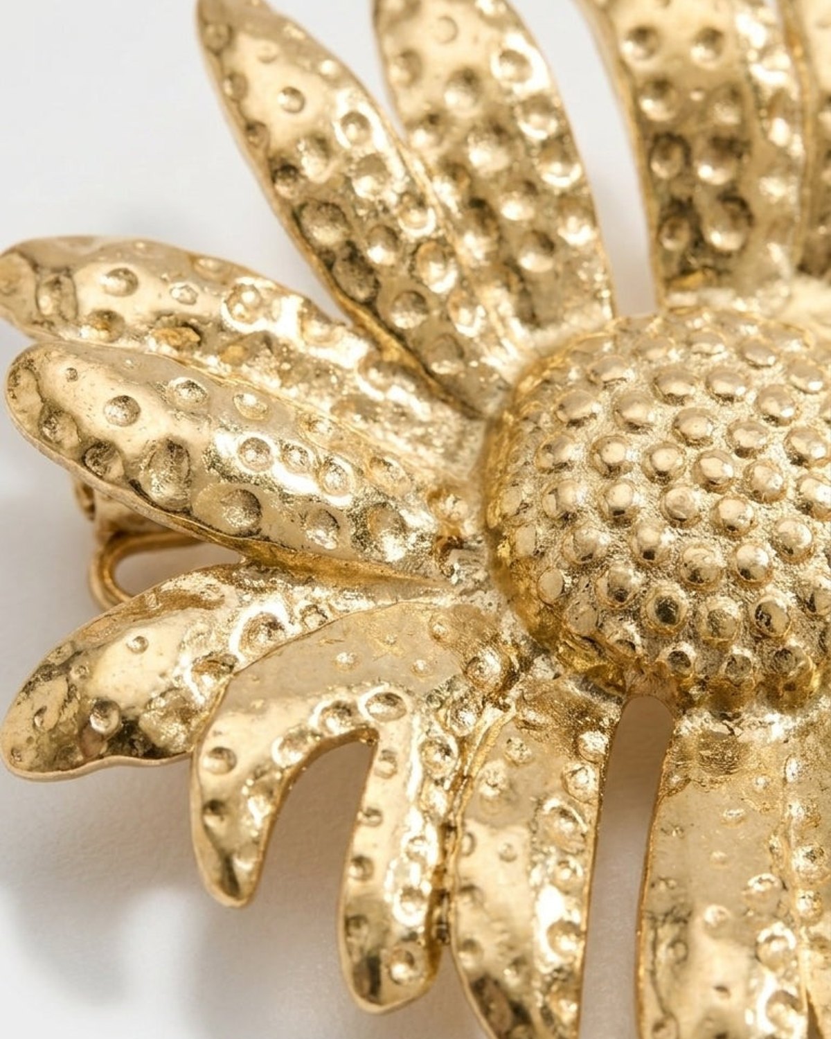 Gold-tone daisy brooch with a textured, dotted surface and dimensional petals, presented on a light background.