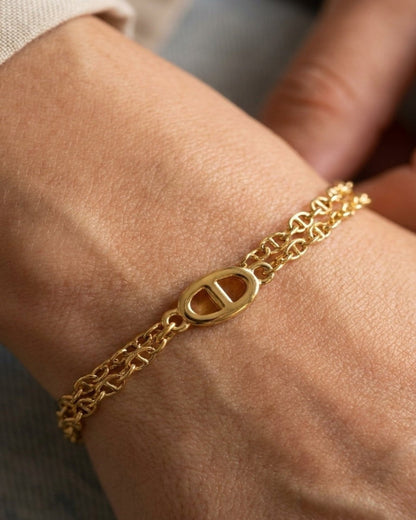 A gold multi-layered anklet with a central oval link worn on a person's leg.