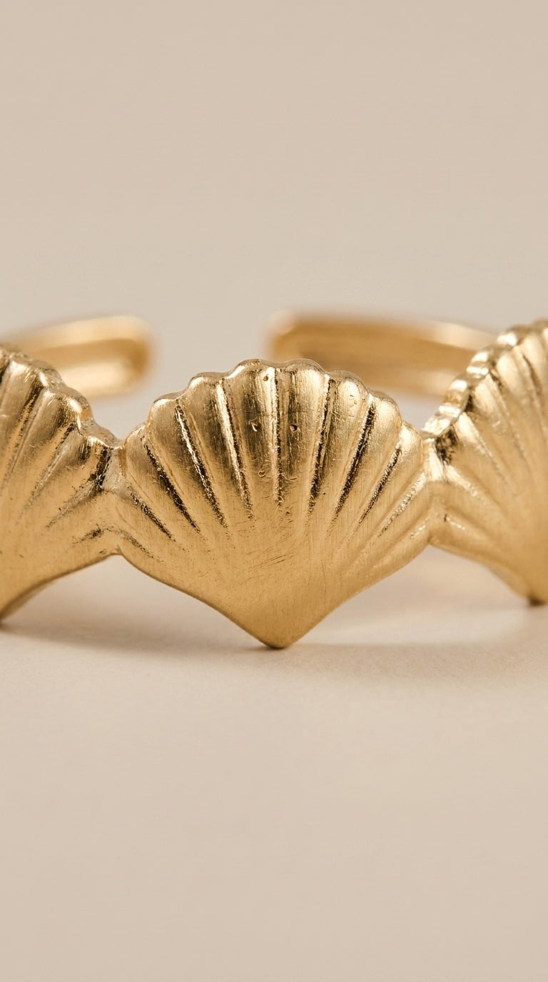 Minimalist gold ring featuring a textured, repeating seashell charm design on a light background.