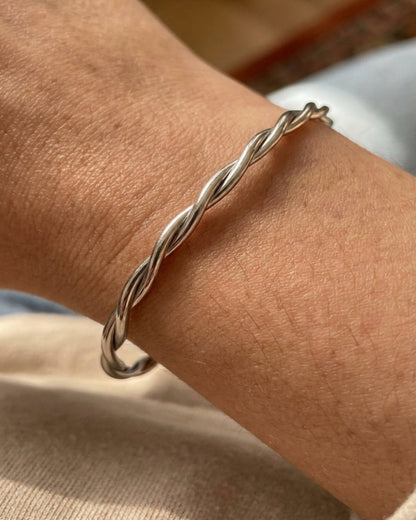A close-up of a thin silver twisted cable bangle bracelet worn on a person's wrist.