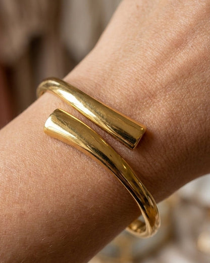 A smooth, polished gold-tone cuff bracelet with overlapping tapered ends worn on a wrist.