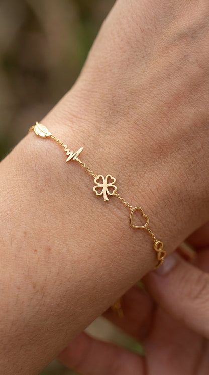 Dainty gold charm bracelet featuring a leaf, heartbeat, four-leaf clover, heart, and infinity symbol on a thin chain.