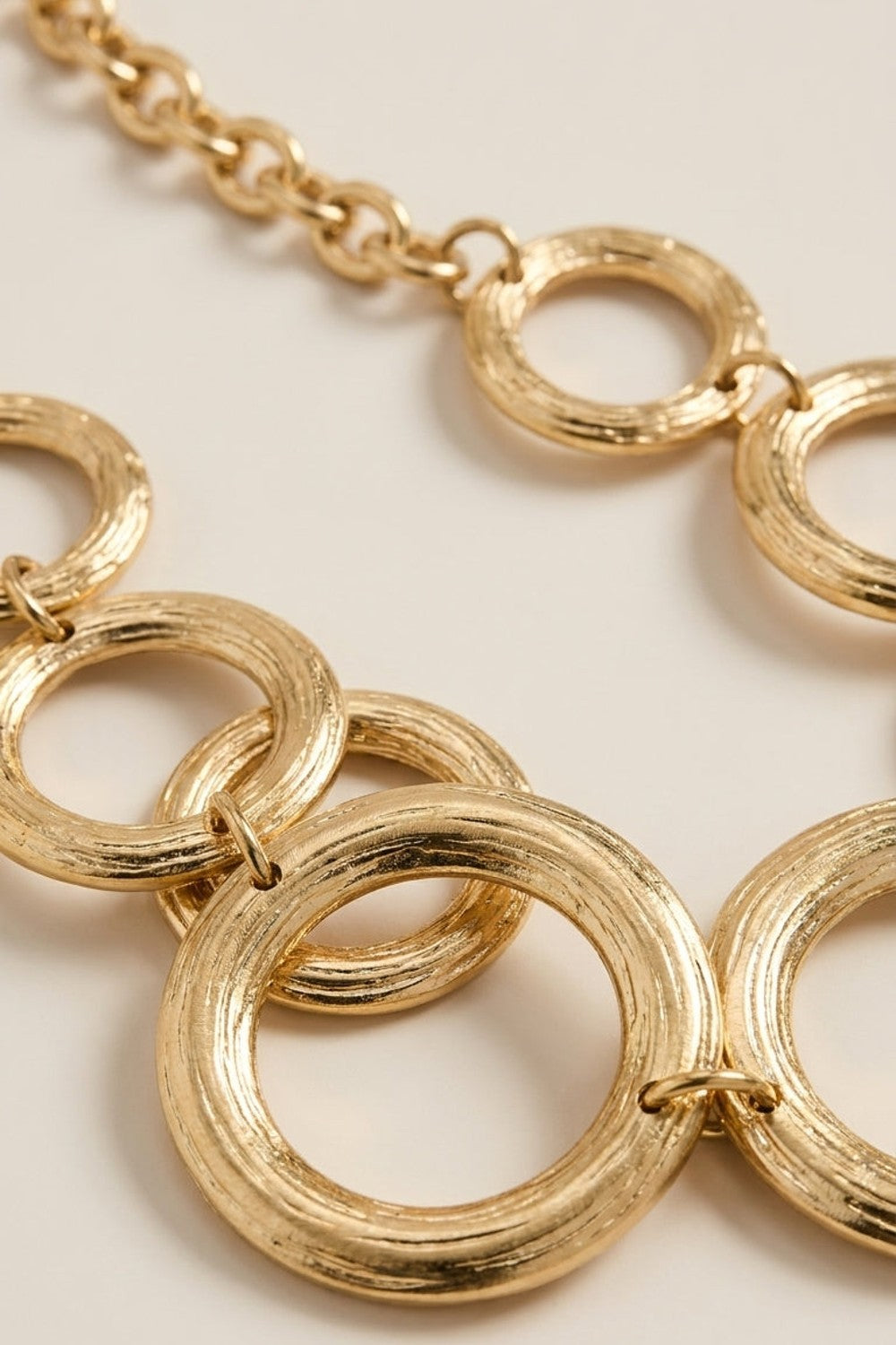 Gilded chain statement necklace featuring interlocking, textured gold rings and a link chain.