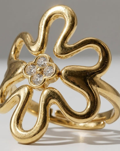 A gold ring featuring a large, stylized openwork flower with four pavé-set stones at its center.
