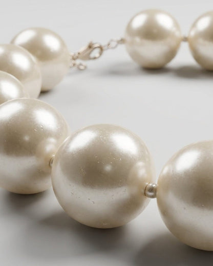 Oversized white pearl choker necklace with a silver clasp on a light grey background.