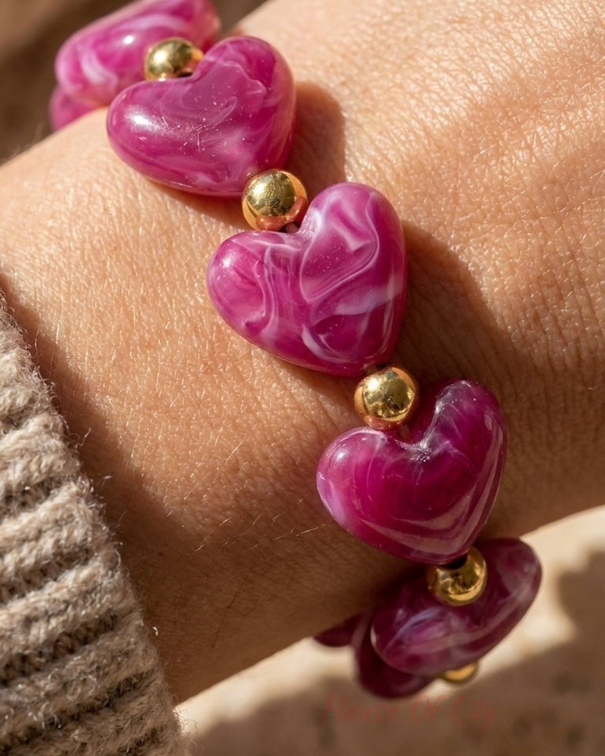 A bracelet of marbled magenta heart beads and small gold spheres on a wrist.