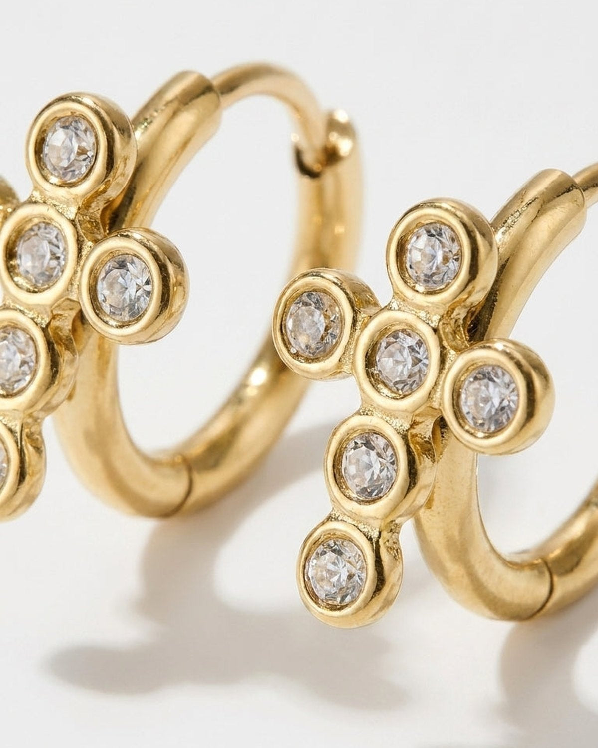 Gold hoop earrings featuring a cross pendant set with clear round rhinestones.