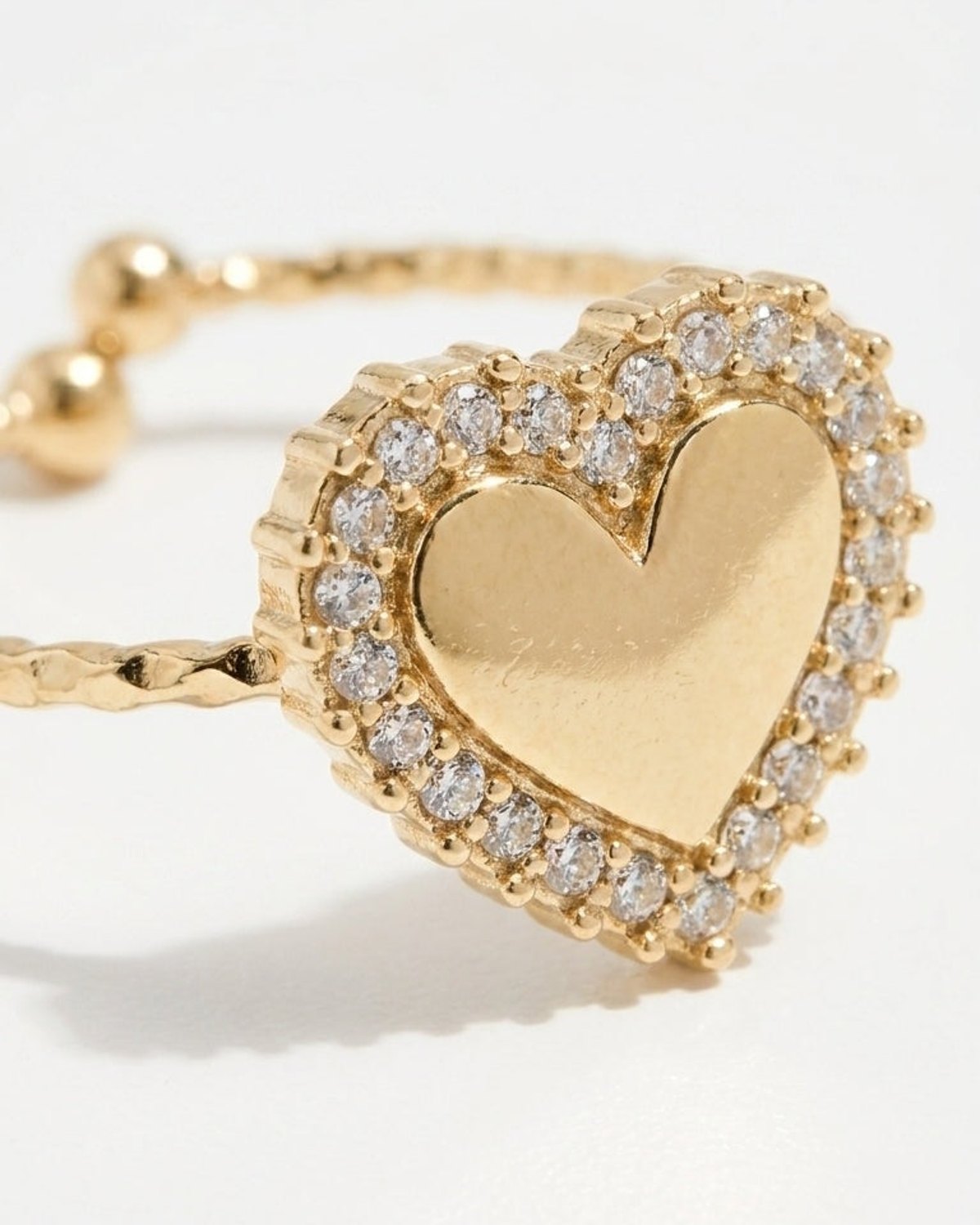 Gold ring featuring a heart-shaped centerpiece paved with clear stones against a plain background.