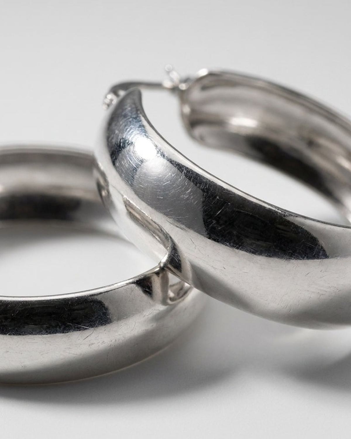 Chunky silver hoop earrings with a polished finish, captured in a close-up against a soft grey background.