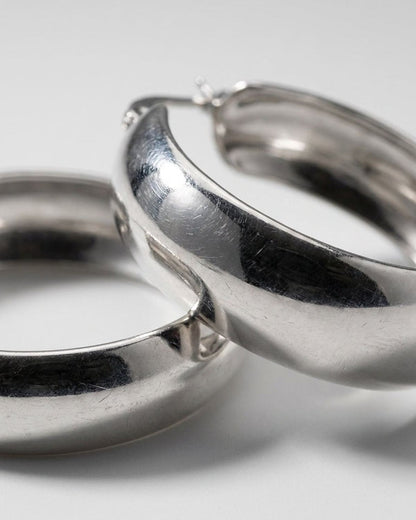 Chunky silver hoop earrings with a polished finish, captured in a close-up against a soft grey background.