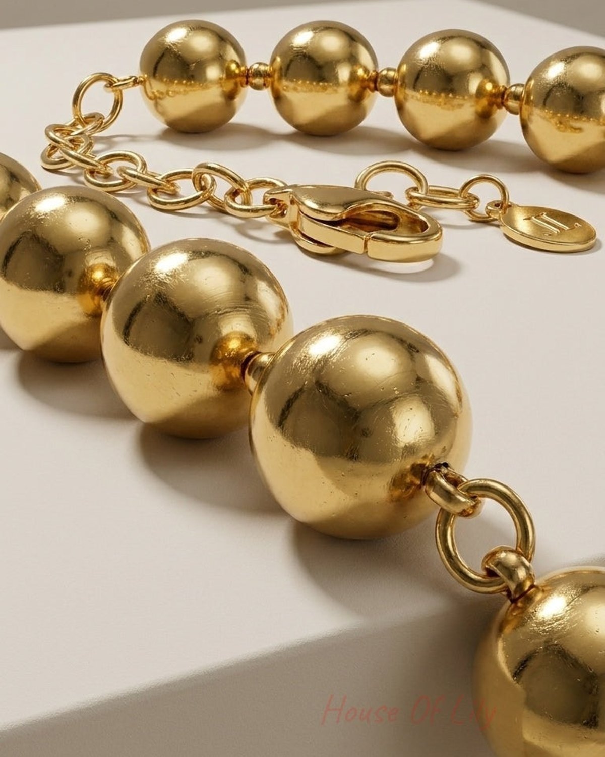 Close-up of a gold-colored beaded chain necklace with large spherical beads and a clasp.
