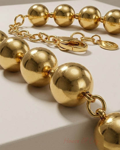 Close-up of a gold-colored beaded chain necklace with large spherical beads and a clasp.