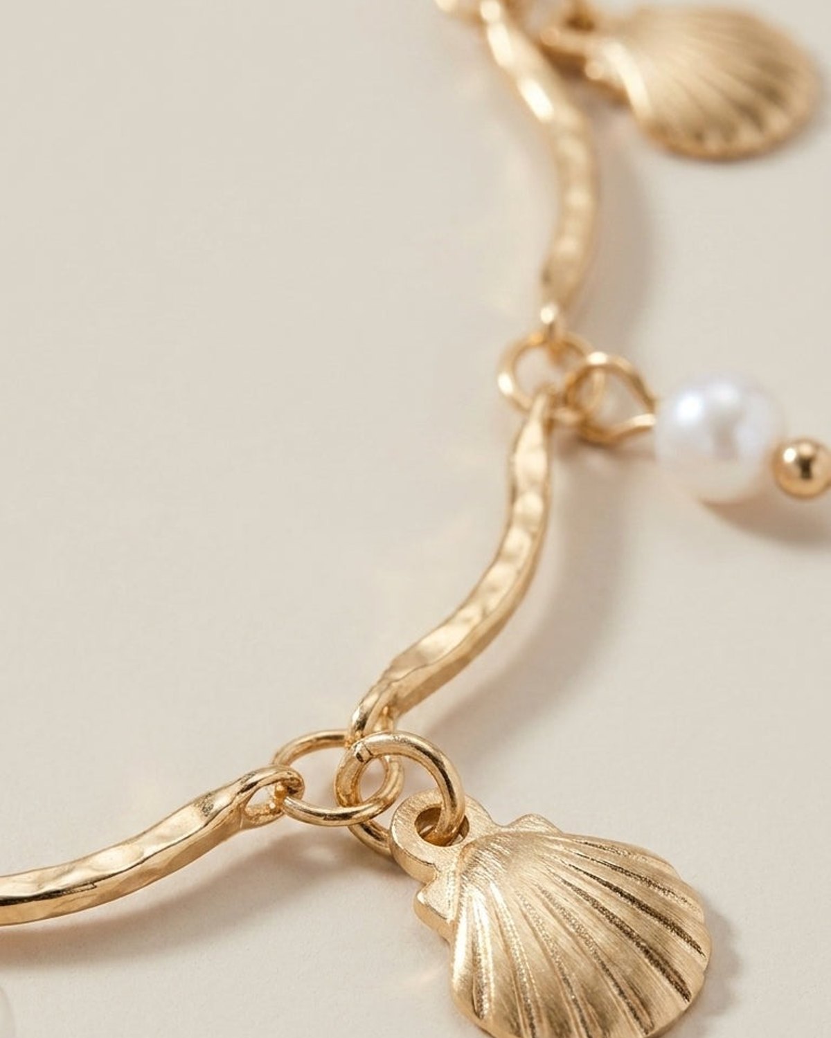 Gold chain necklace with a wavy texture, dangling seashell charms and white pearls.