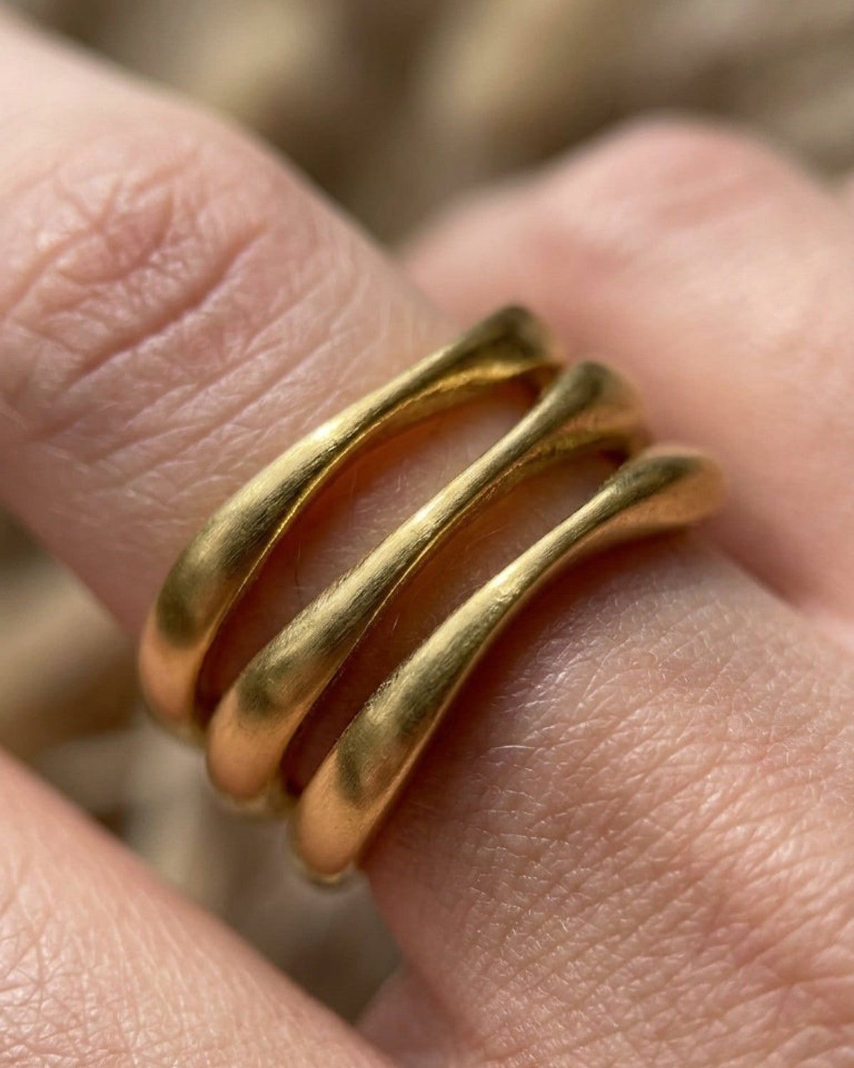 Gold wave stack ring with three organic, undulating bands worn on a finger.