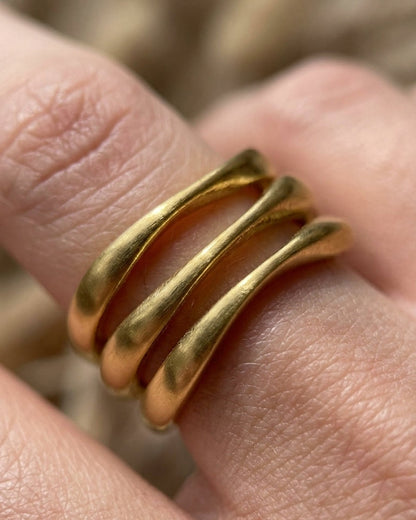 Gold wave stack ring with three organic, undulating bands worn on a finger.