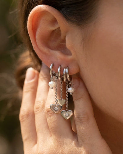 Silver Heart Zircon Drop Earrings worn on a pierced ear, featuring hanging chains, hearts, and pearls.