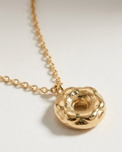 A gold-colored donut-shaped pendant hangs from a matching delicate chain on a neutral background.