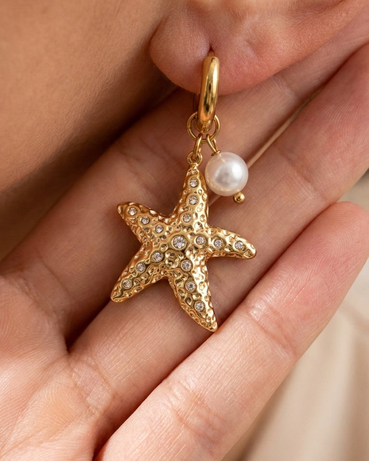 Gold hoop earring featuring a textured starfish charm with embedded crystals and a dangling white pearl.