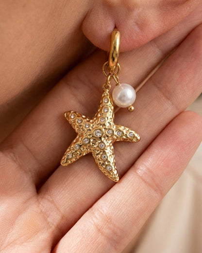 Gold hoop earring featuring a textured starfish charm with embedded crystals and a dangling white pearl.