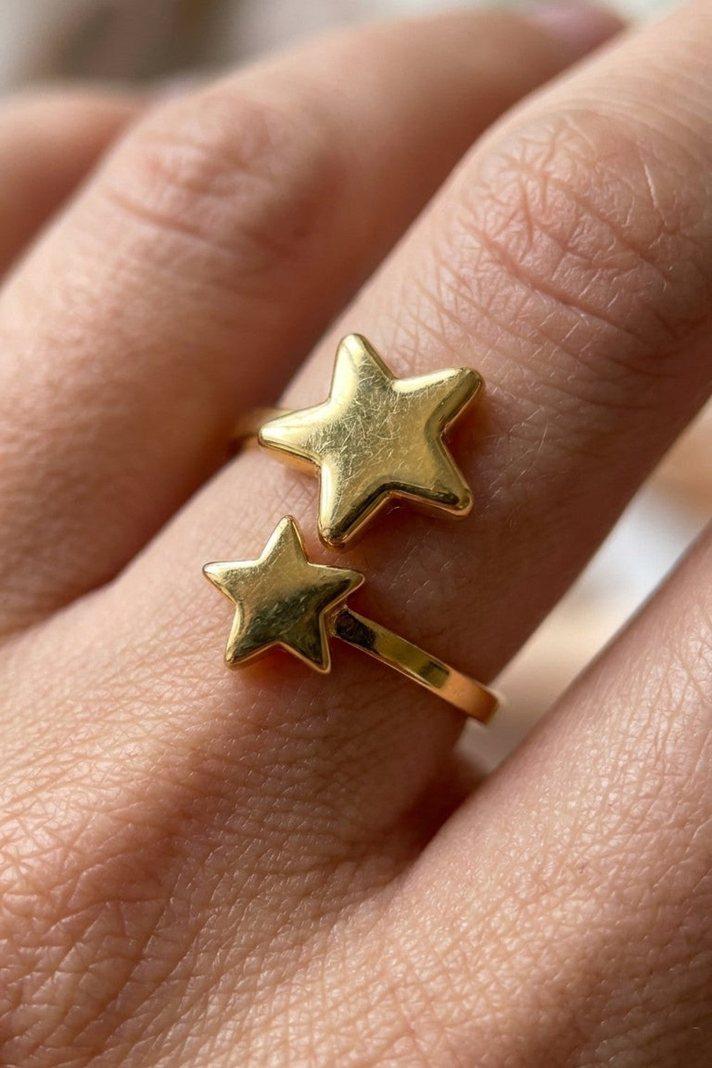 Gold minimalist ring featuring two unjoined star motifs of different sizes on a finger.