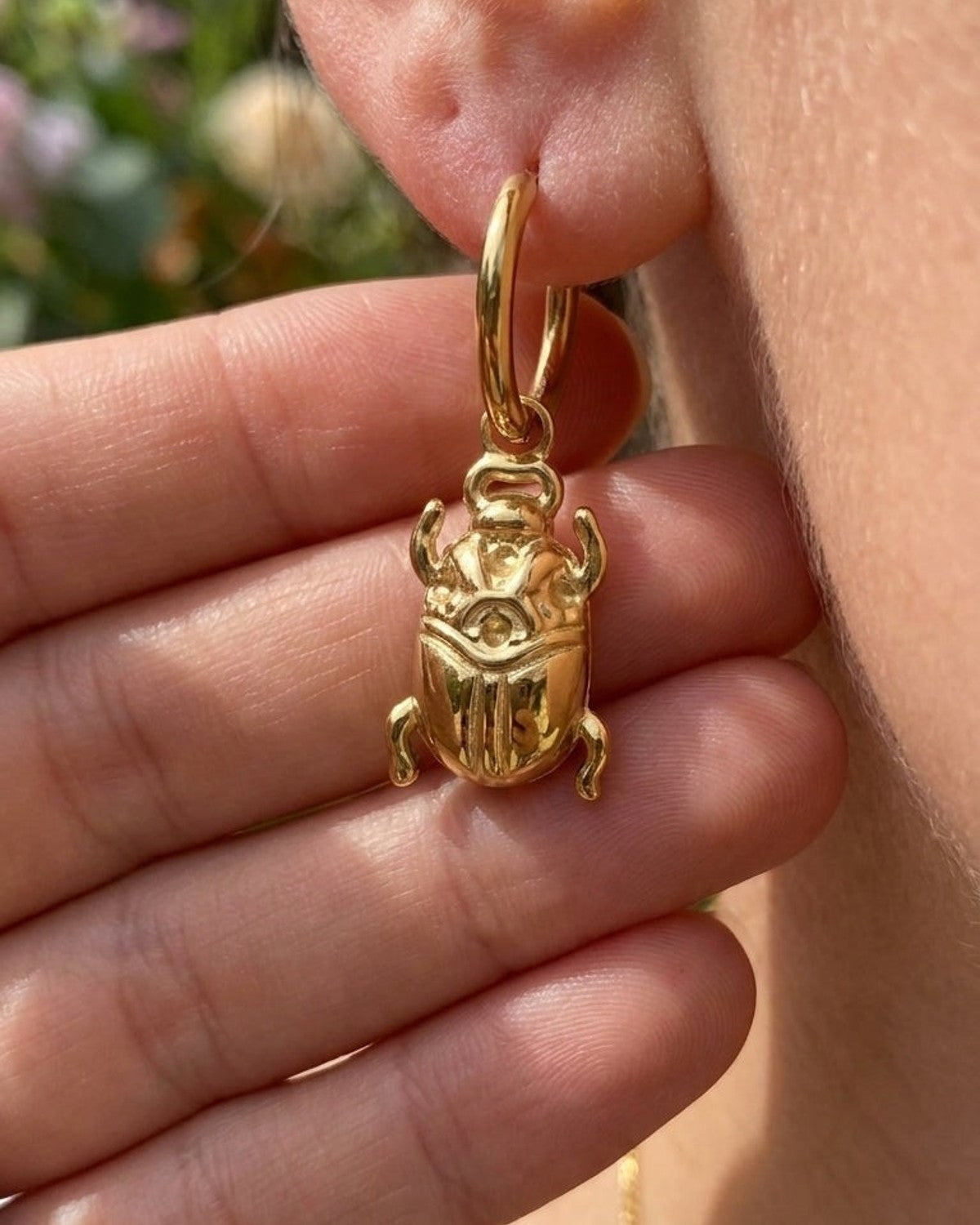 House Of Lily gold drop earrings featuring a polished beetle pendant on a small hoop, worn on an earlobe.