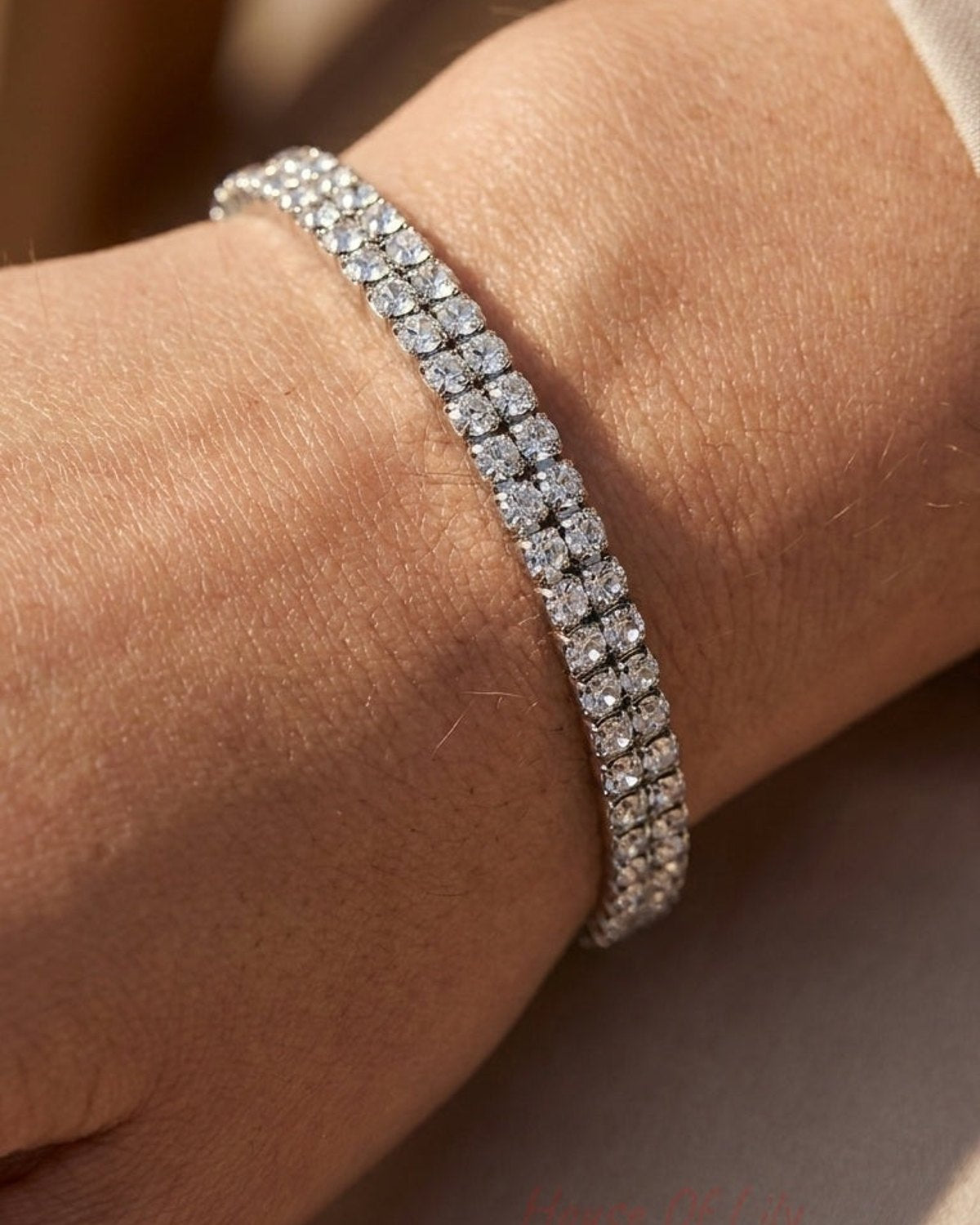 A double-strand silver tennis bracelet adorned with sparkling clear round-cut crystals worn on a wrist.
