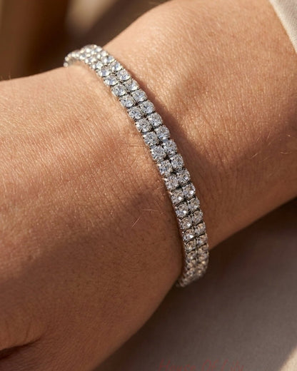 A double-strand silver tennis bracelet adorned with sparkling clear round-cut crystals worn on a wrist.
