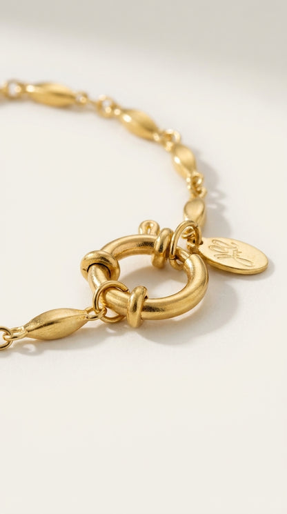 Brushed gold oval link chain bracelet with a round clasp and small engraved tag.