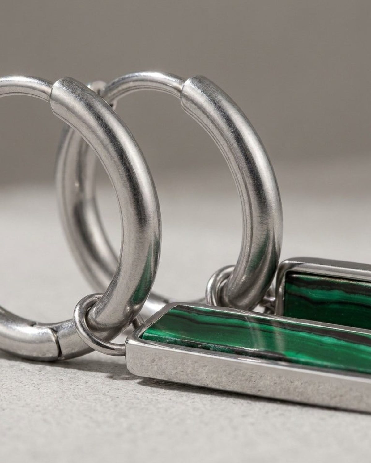Silver hoop earrings with hanging rectangular green gemstone bars featuring banded patterns.