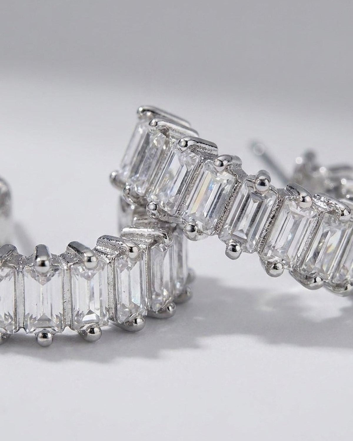 Silver hoop earrings set with a continuous row of clear, rectangular baguette-cut stones.