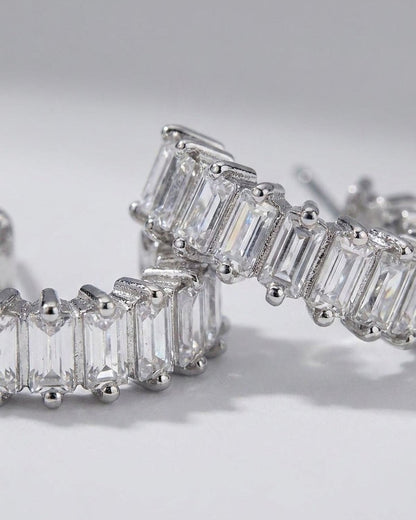 Silver hoop earrings set with a continuous row of clear, rectangular baguette-cut stones.