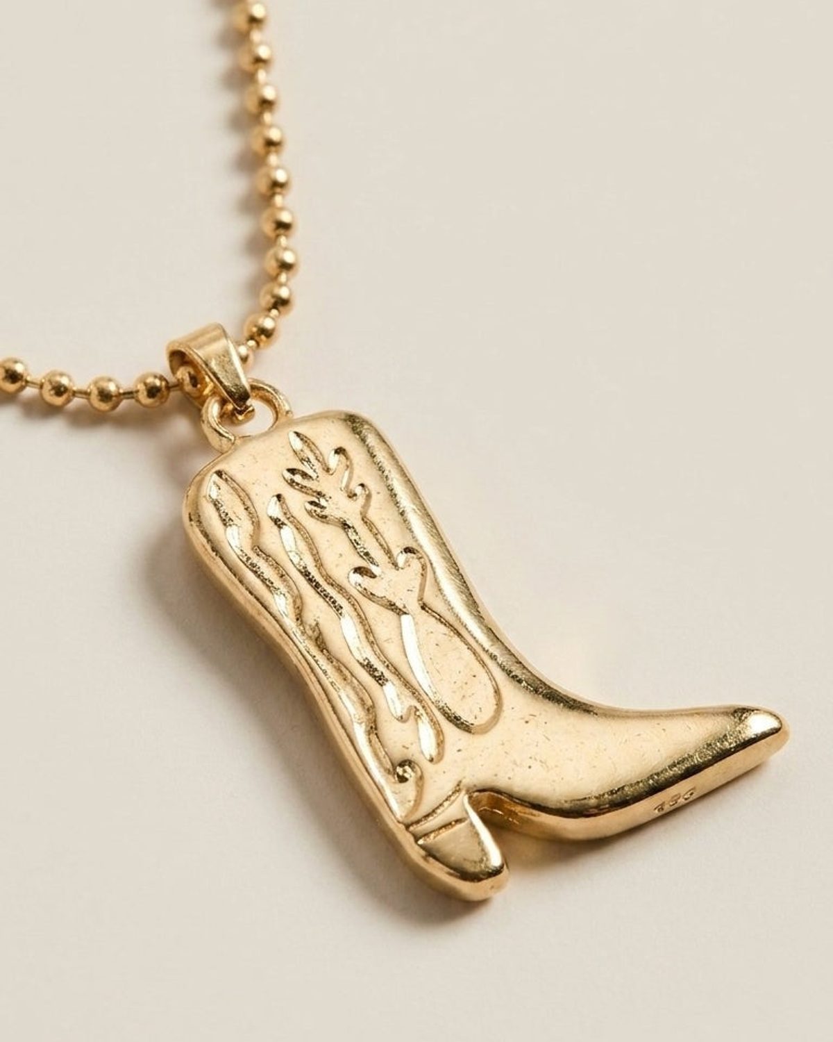 Gold ball chain necklace featuring a textured, engraved cowboy boot pendant on a light background.