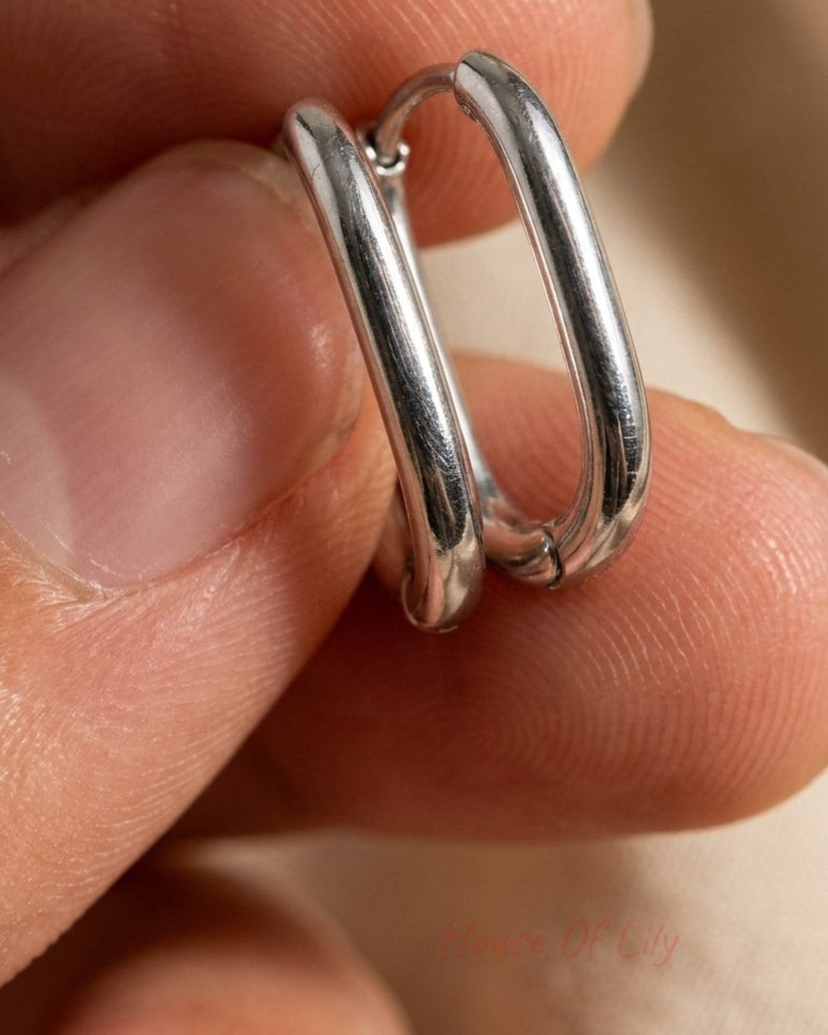 Small silver rectangular hoop earrings held between fingers, minimalist House of Lily design with a polished finish.
