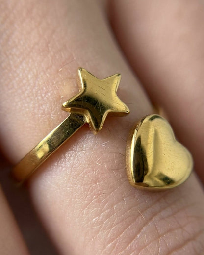 Gold-finish ring featuring a star and a heart shape worn on a finger.