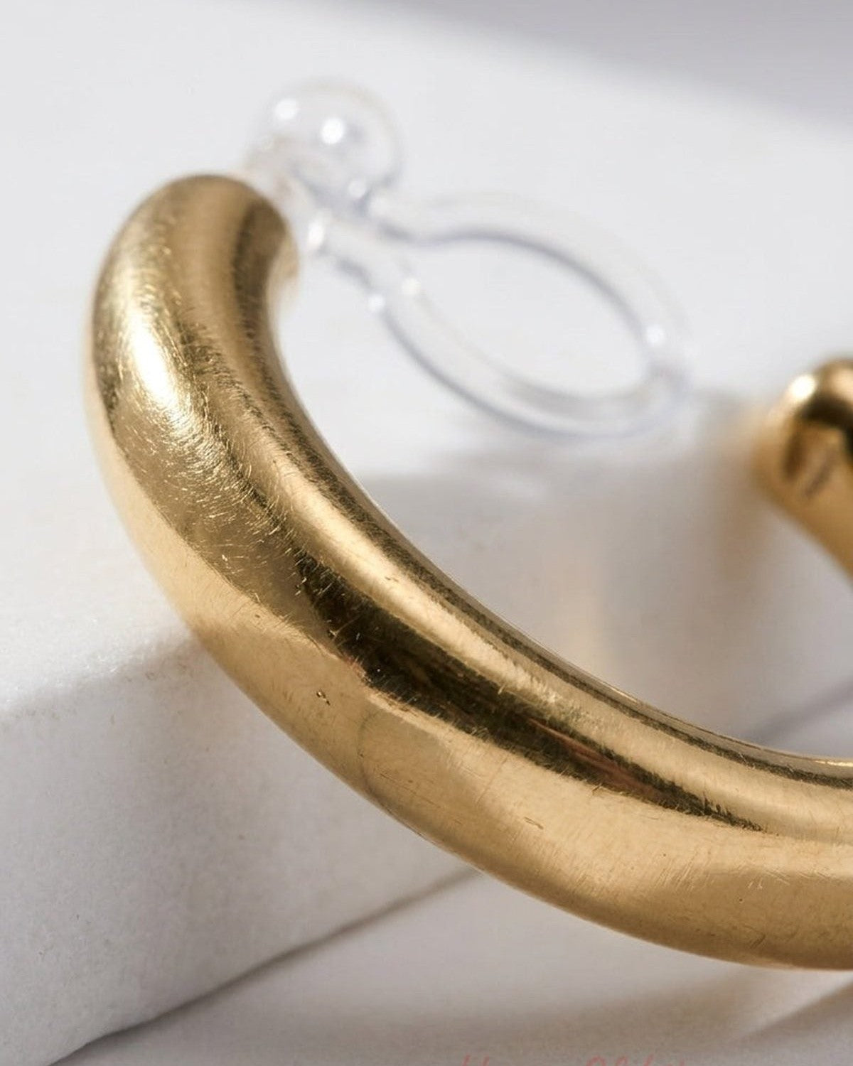 Thick, brushed gold-tone hoop clip-on earring resting on a white surface.
