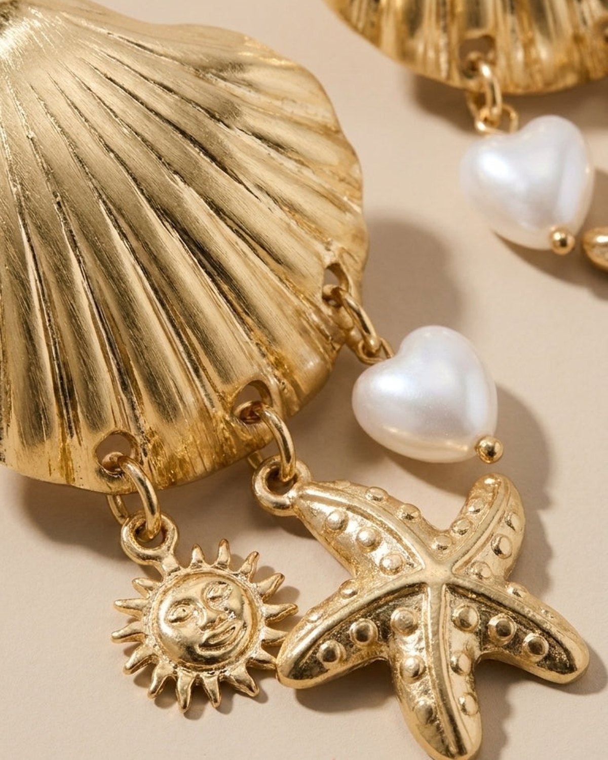 Gold shell earrings featuring dangling heart-shaped faux pearls, a starfish, and a sun charm.