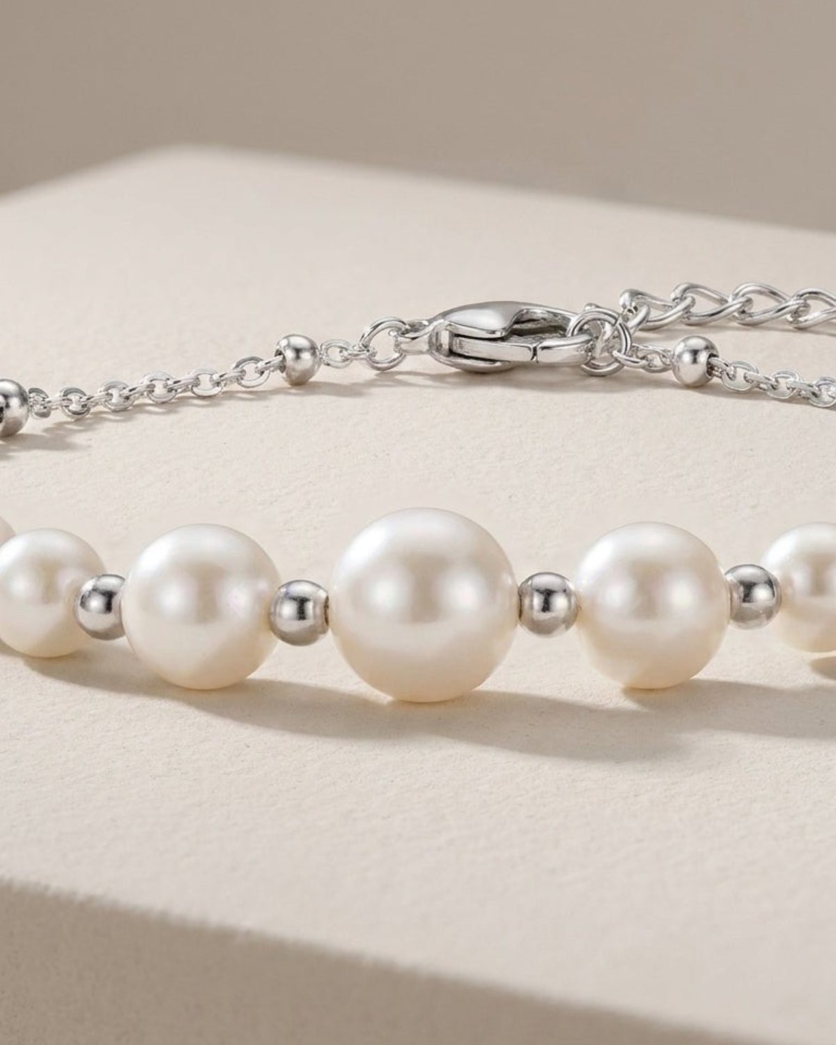 Silver bracelet featuring round white pearls and small metal spacer beads, displayed on a neutral surface.