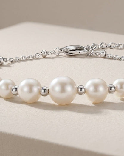 Silver bracelet featuring round white pearls and small metal spacer beads, displayed on a neutral surface.