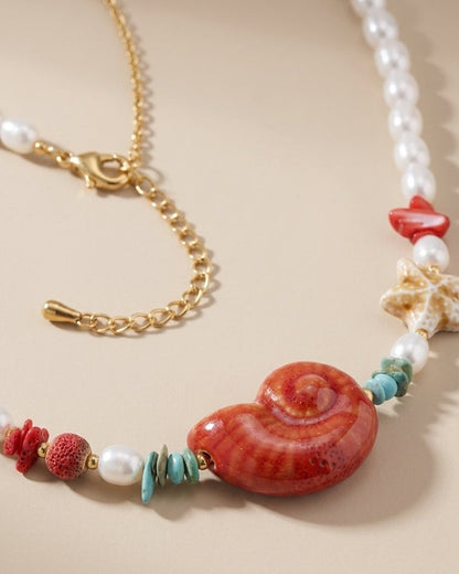 A seashell necklace with white pearls, a large red shell pendant, a starfish, and turquoise and coral-toned beads.