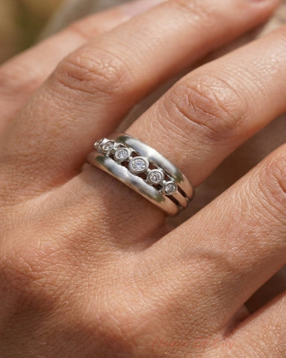 A silver ring with bezel-set rhinestones sits on a hand.