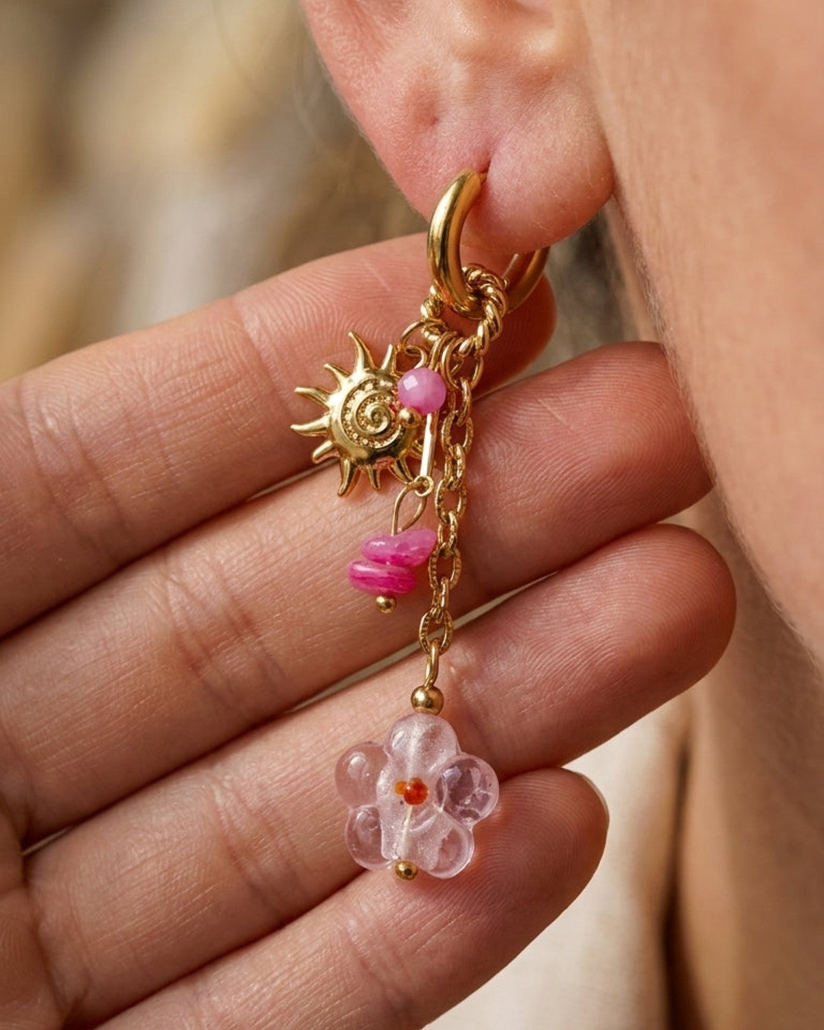 Gold hoop earring with dangling gold chain charms, a sunburst pendant, pink beads, and a light pink glass flower.