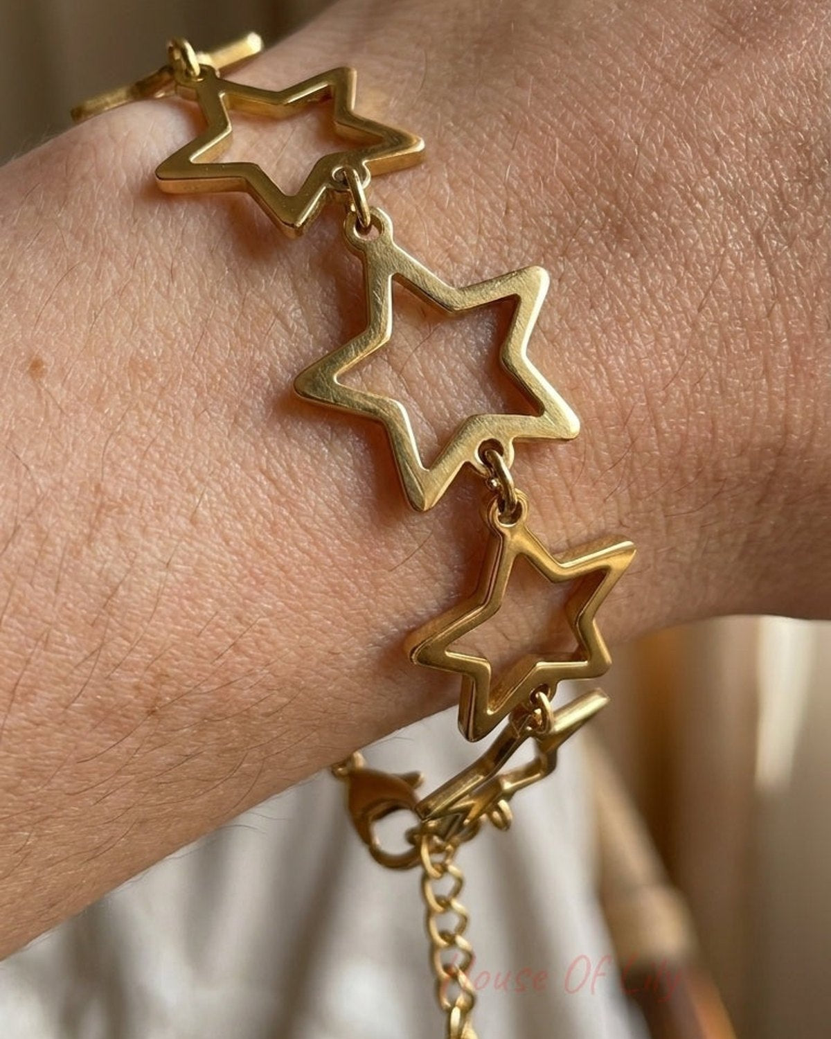 A gold-toned metal bracelet featuring linked open star charms worn on a wrist.