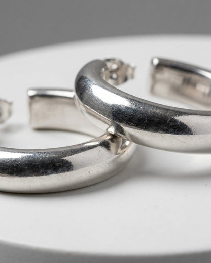 Thick silver hoop earrings with a polished, minimalist design, resting on a white surface.