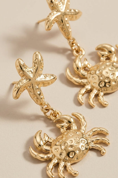 Gold drop earrings with a textured starfish stud and a dangling textured crab charm.