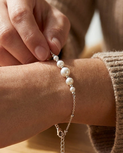 Silver bracelet with graduated white pearls on a wrist, featuring a delicate chain and adjustable clasp.